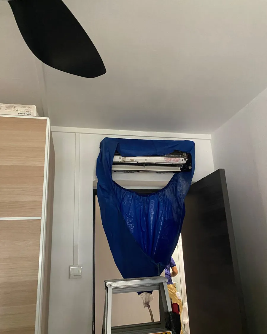 Aircon wall unit opened with a blue service cradle hung beneath it in a Singapore bedroom