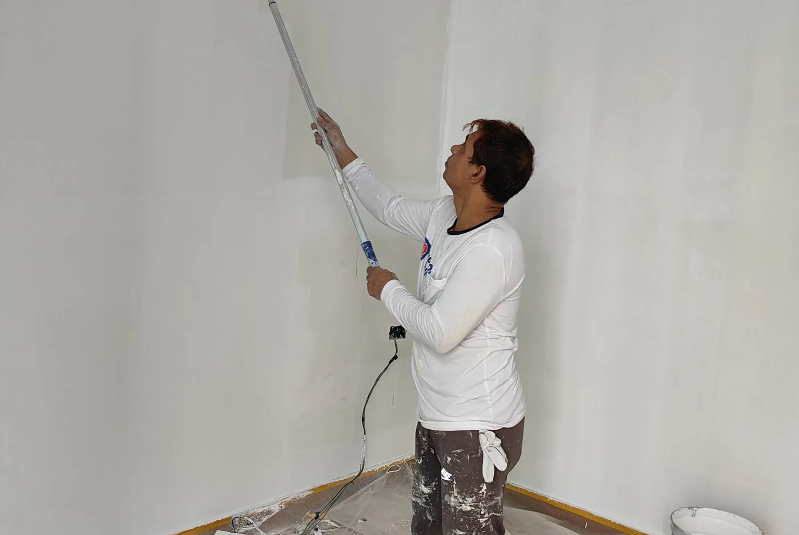 Painter rolling a ceiling with an extension pole in a Singapore flat
