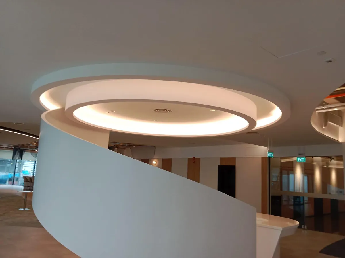 Two-tier circular false ceiling with warm cove lighting above a reception area in Singapore