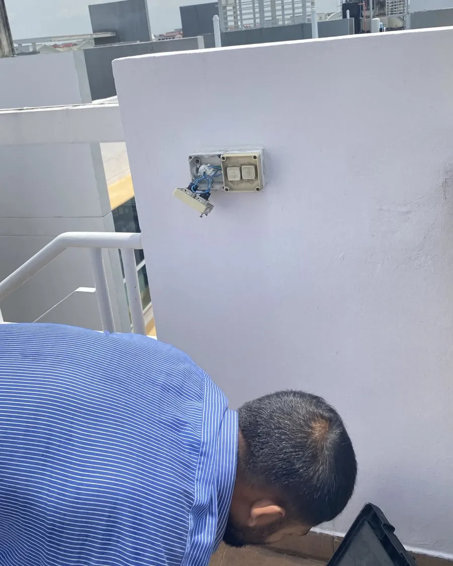 Electrician wiring an outdoor switch plate on an exterior wall in Singapore