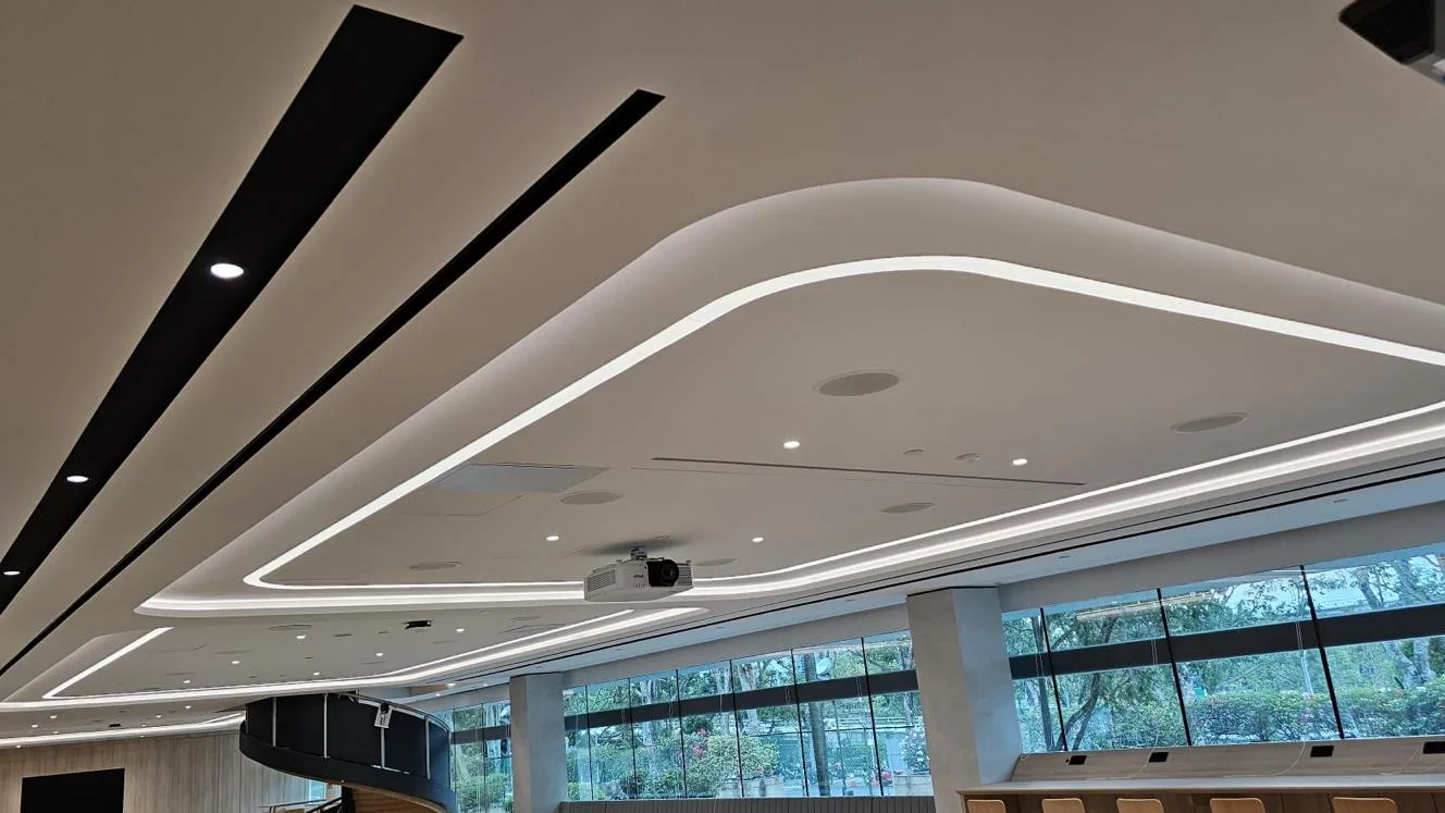 Curved false ceiling with recessed cove lighting above an office floor in Singapore