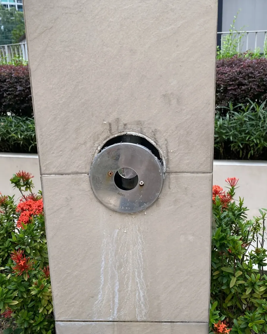 Outdoor shower valve running water down a tiled wall at a Singapore condominium