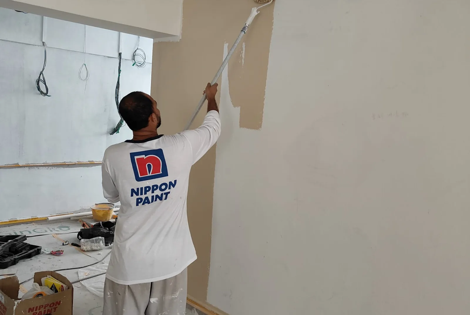 Painter in a Nippon Paint shirt rolling a wall in a Singapore flat