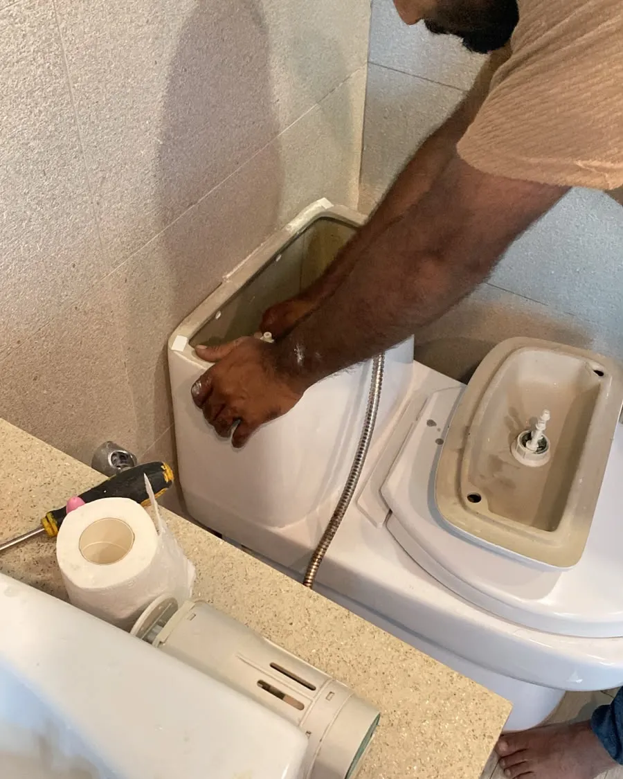 Plumber replacing the flush valve inside a toilet cistern in a Singapore bathroom