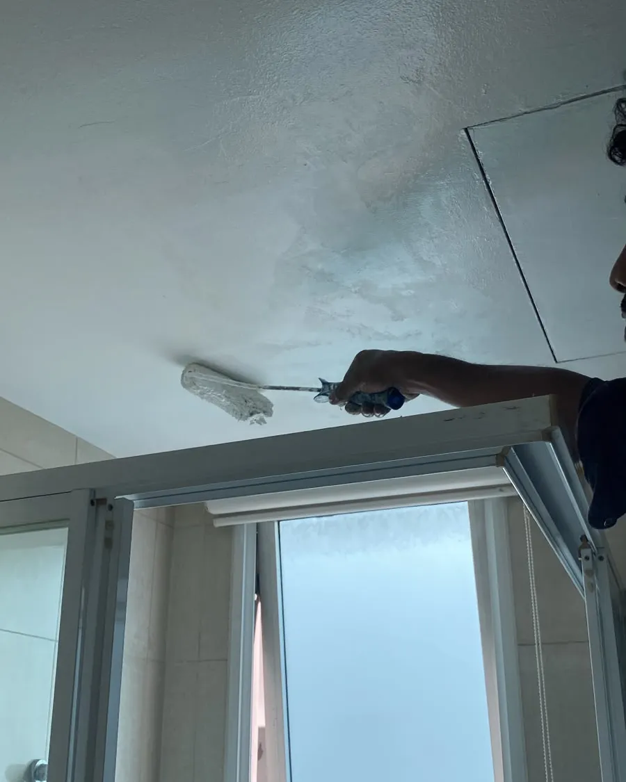 Roller on an extension pole applying paint to a toilet ceiling in Singapore
