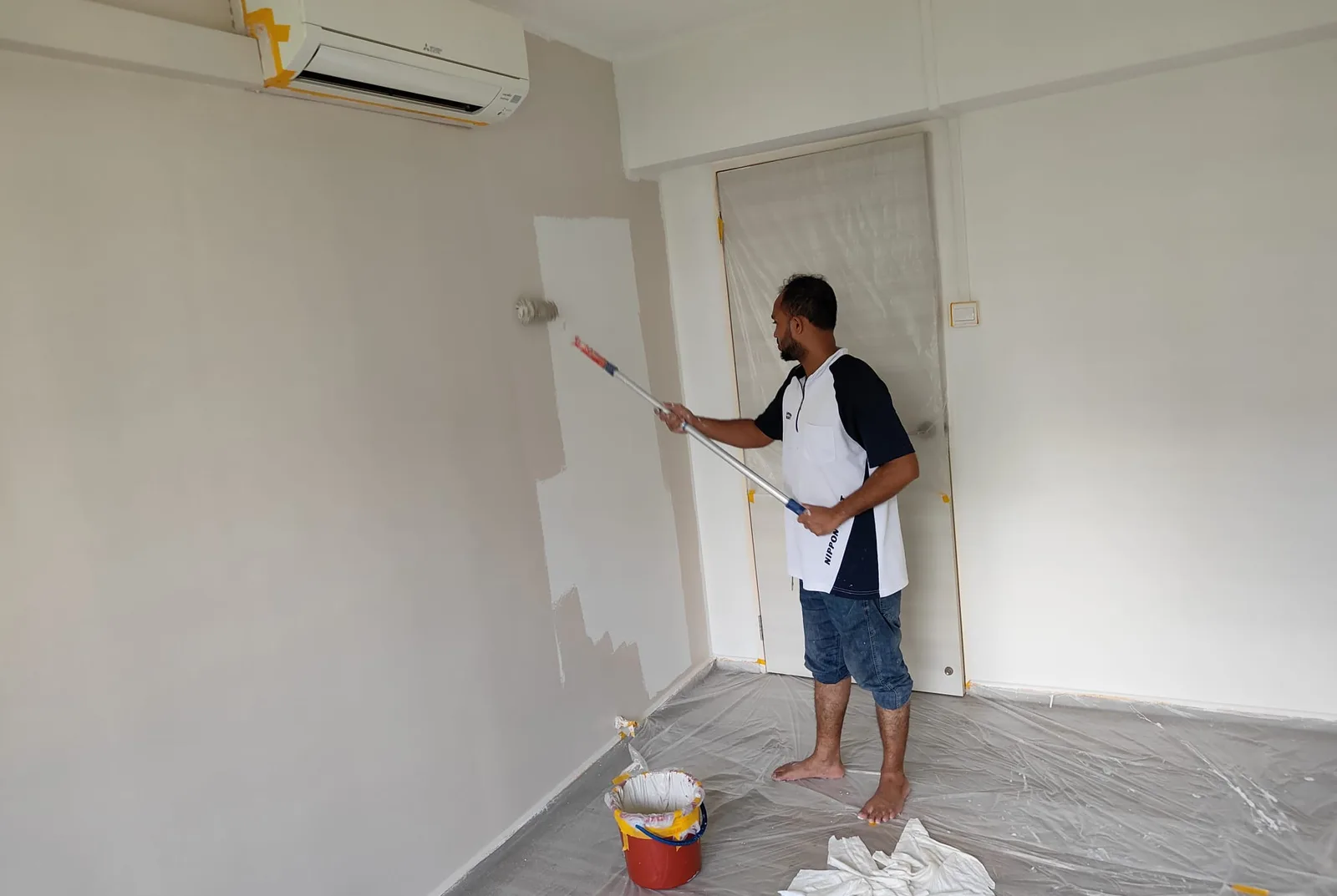 Painter rolling a single patched wall in a Singapore bedroom with the floor sheeted